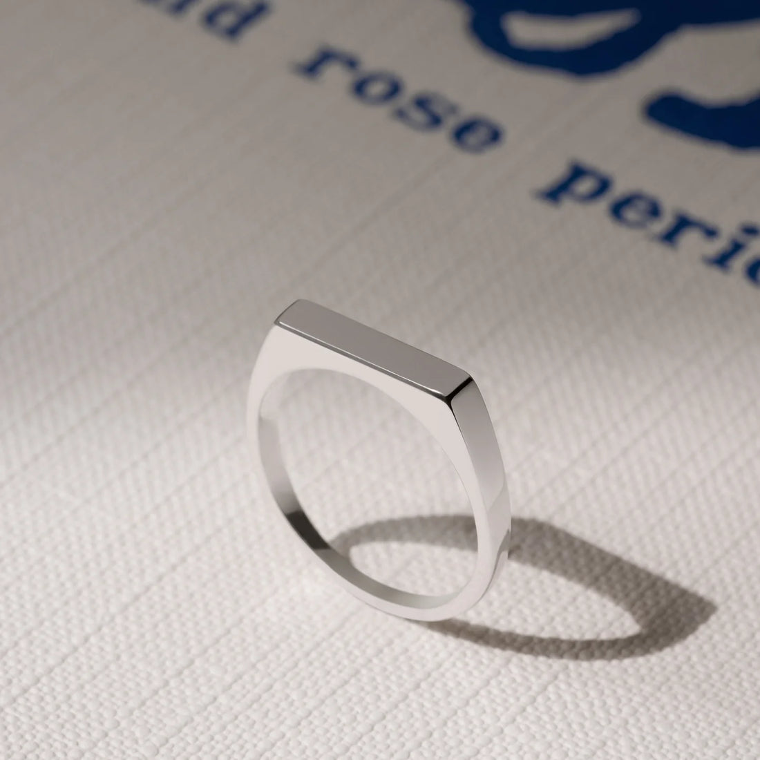 Silver ring on a textured white surface with blue text in the background