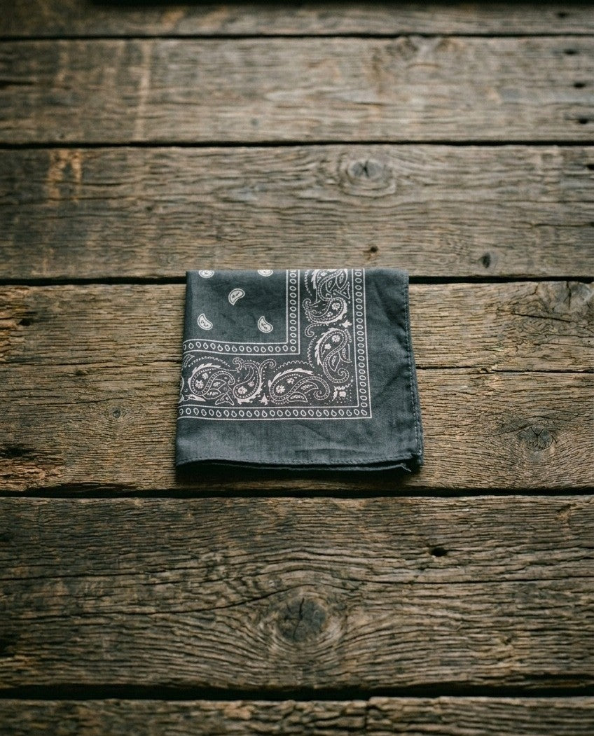 Slate gray square bandana with white paisley pattern folded on a dark weathered wood surface – Dazzle classic collection