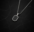 Silver necklace with a black hexagonal pendant on a dark textured background