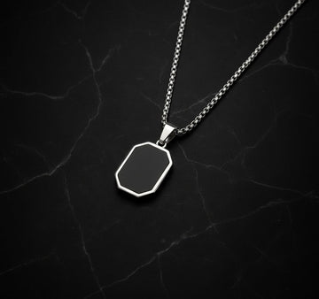 Silver necklace with a black hexagonal pendant on a dark textured background