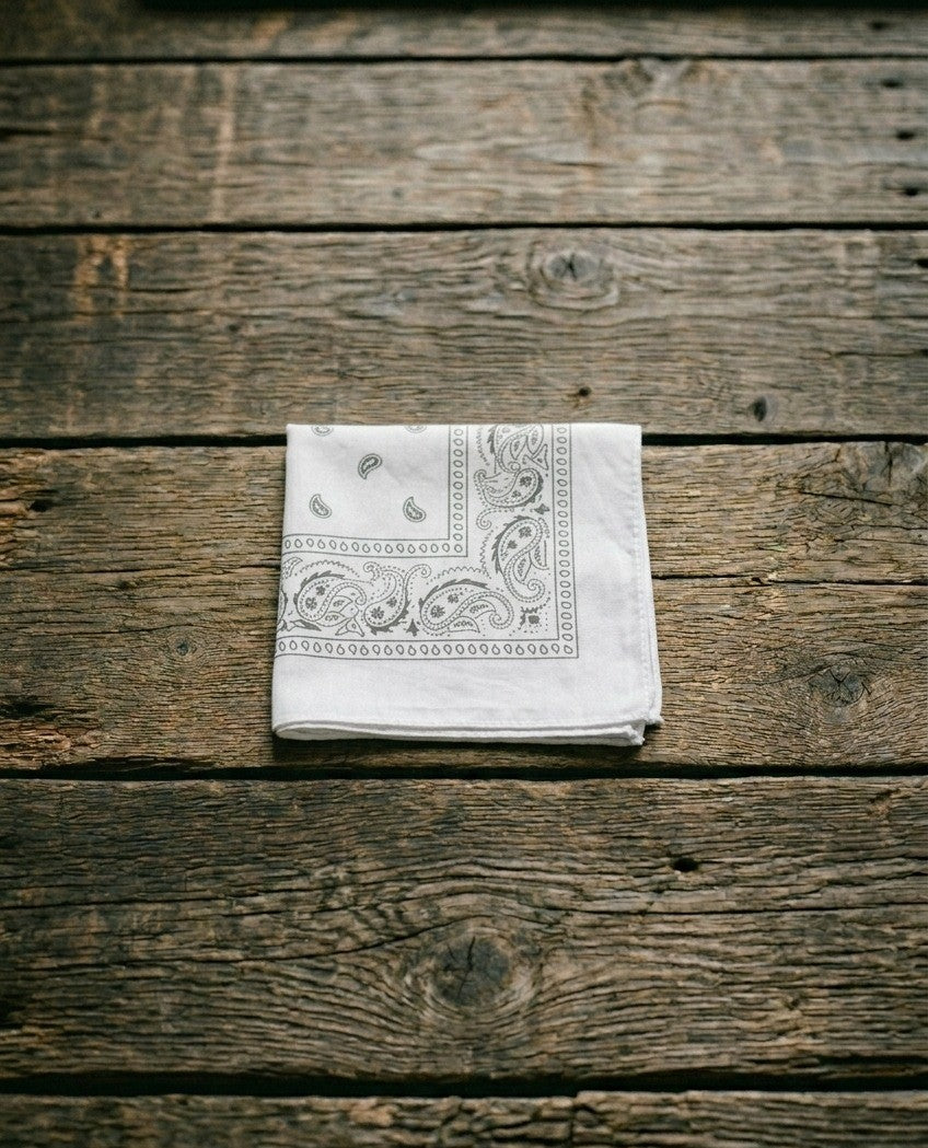 Crissh white cotton bandana featuring a detailed black paisley design folded on a rustic wood background – Dazzle unisex fashion.