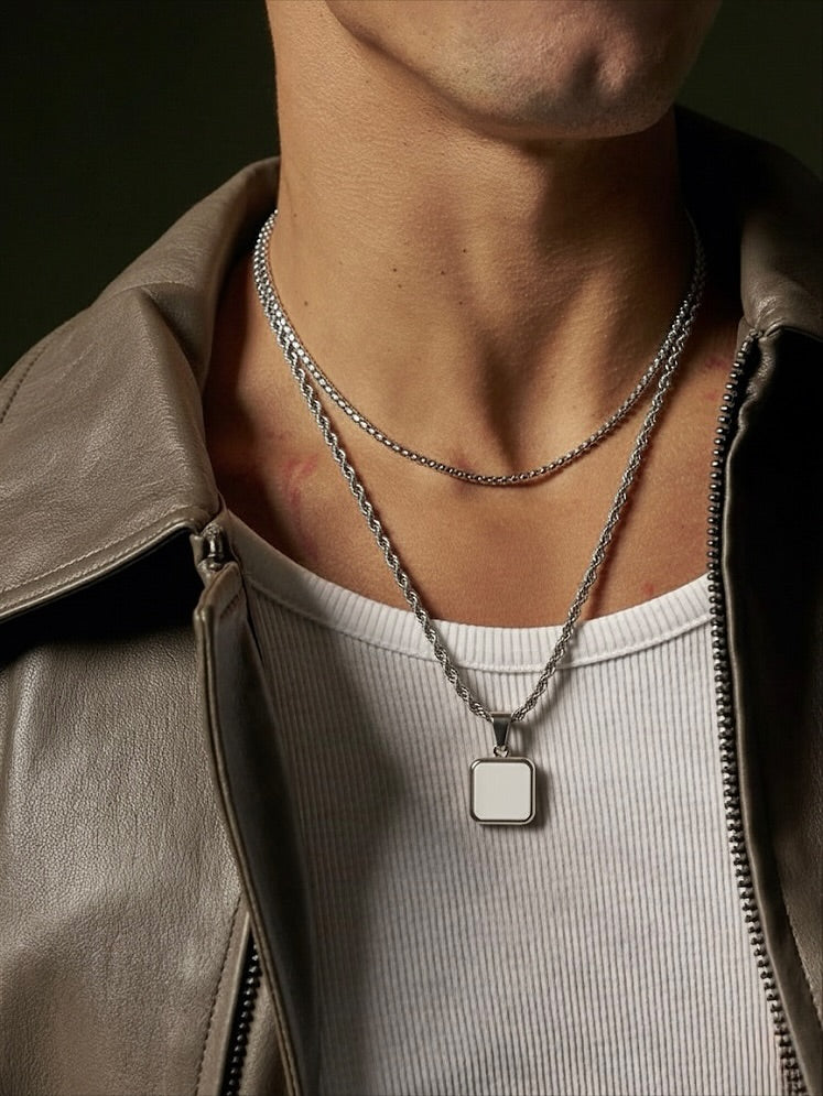 Person wearing a silver necklace with a square pendant against a dark background