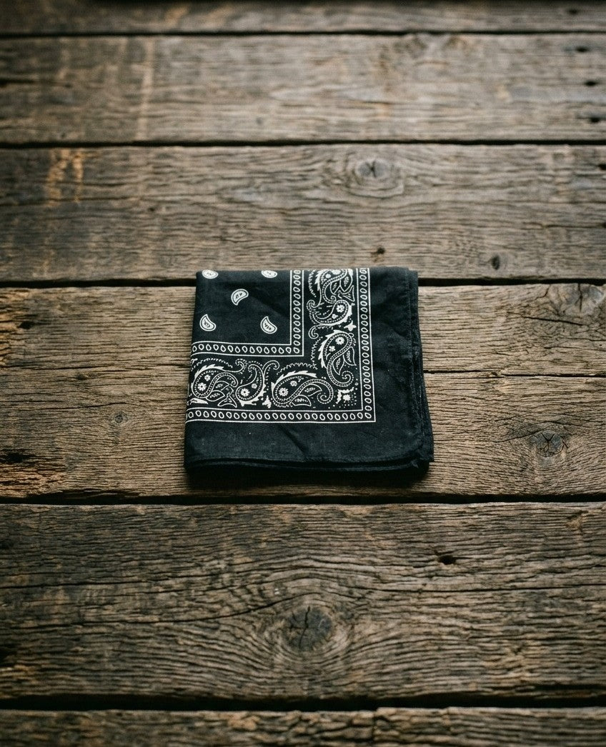 Midnight black premium cotton bandana with white paisley details folded on an organic wood plank background – Dazzle fashion accessories.