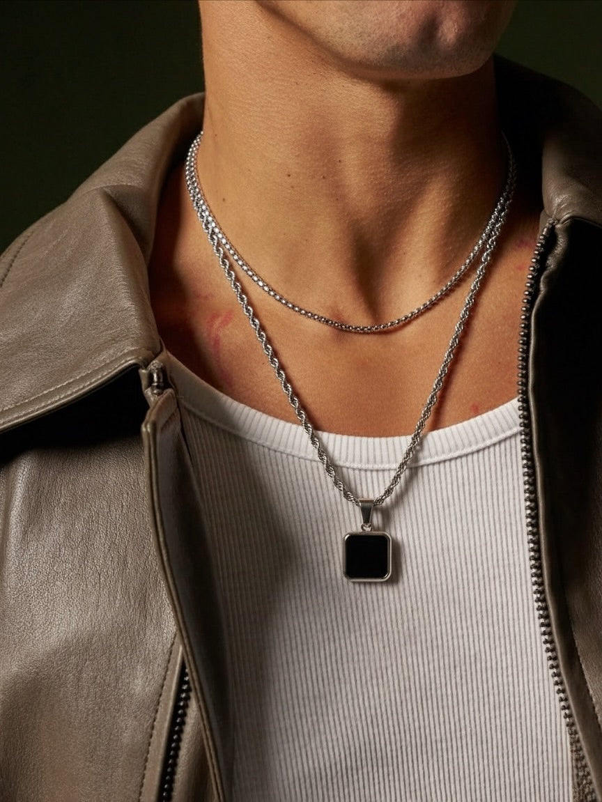Person wearing a silver necklace with a black pendant, close-up on neck and chest.