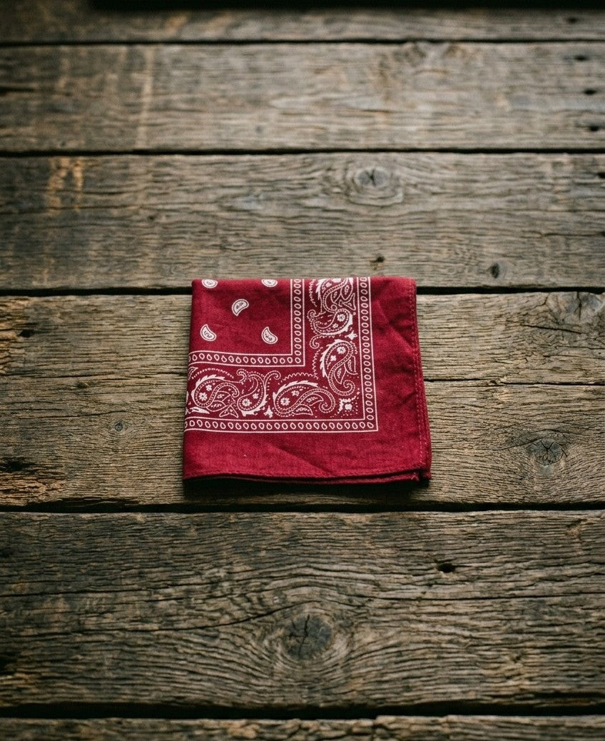 Crimson red cotton paisley bandana folded neatly on a rustic wooden tabletop background – Dazzle streetwear accessories