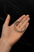 Hand holding a silver bracelet against a black background