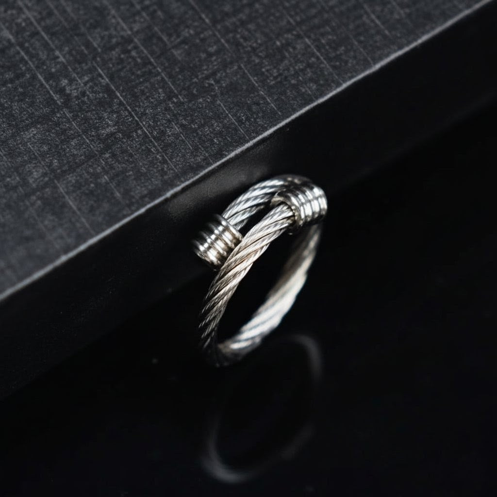 Silver ring with braided design on a black textured surface