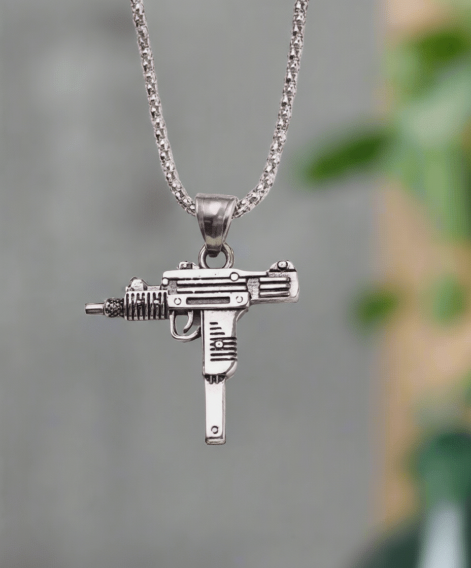 Silver gun-shaped pendant on a chain against a blurred green and gray background